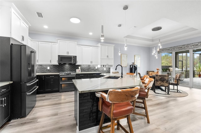 kitchen with sink, pendant lighting, a center island with sink, appliances with stainless steel finishes, and light wood-type flooring