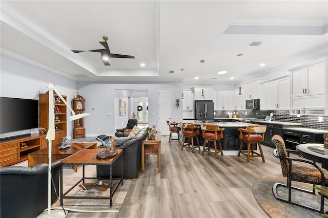 living room with a tray ceiling, light hardwood / wood-style flooring, ceiling fan, and crown molding