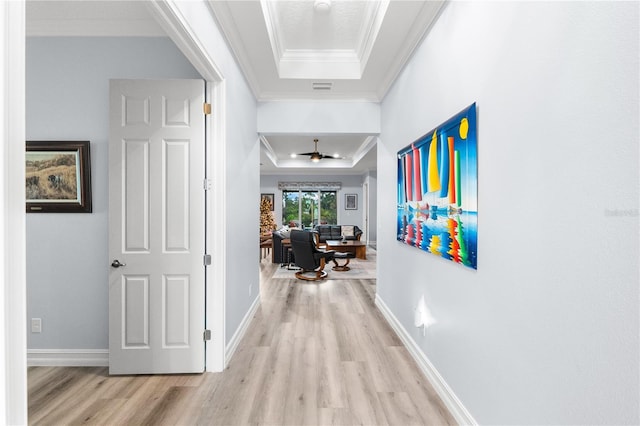 hall with a tray ceiling, crown molding, and light wood-type flooring