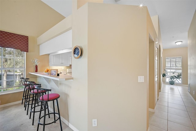 kitchen with a kitchen bar, kitchen peninsula, white cabinetry, and plenty of natural light