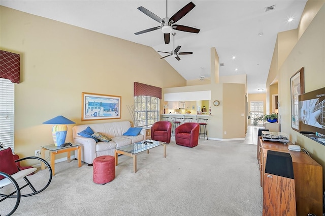 carpeted living room with ceiling fan, plenty of natural light, and high vaulted ceiling