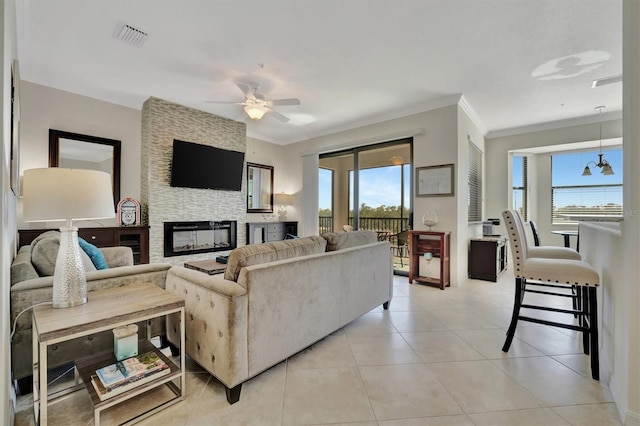 tiled living room with a fireplace, ceiling fan with notable chandelier, crown molding, and a wealth of natural light