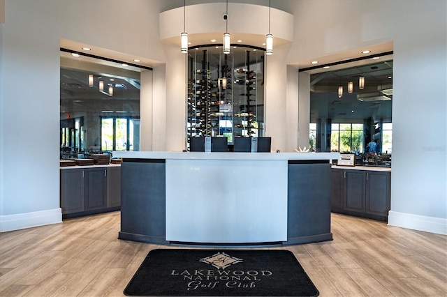 bar with decorative light fixtures, a towering ceiling, and light hardwood / wood-style flooring