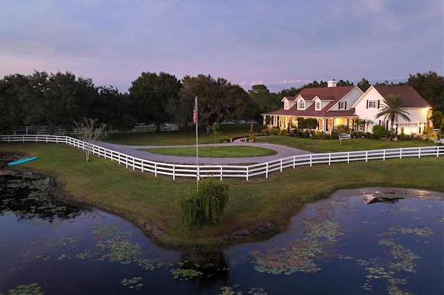 back house at dusk featuring a rural view, a water view, and a lawn