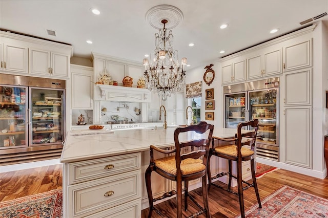 kitchen with a kitchen island with sink, wine cooler, light hardwood / wood-style flooring, decorative light fixtures, and stainless steel appliances