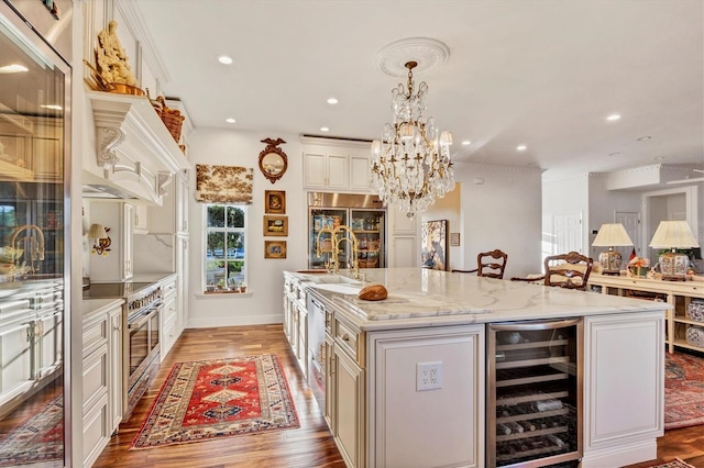 kitchen with high quality appliances, a kitchen island with sink, wine cooler, light wood-type flooring, and decorative light fixtures