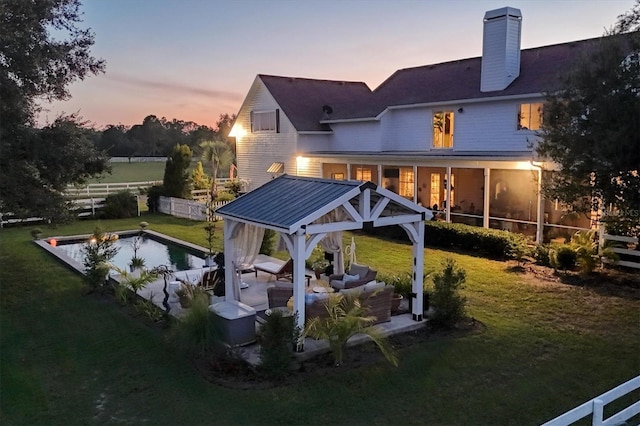 back house at dusk with outdoor lounge area, a sunroom, a gazebo, and a yard