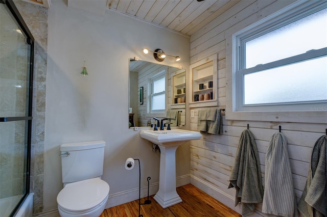 full bathroom with wooden ceiling, wood walls, wood-type flooring, combined bath / shower with glass door, and toilet