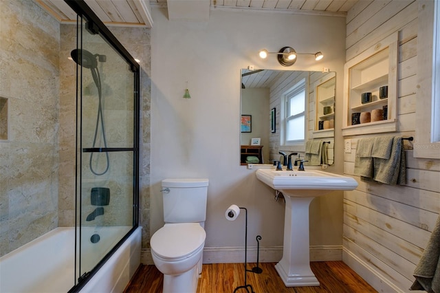 full bathroom featuring bath / shower combo with glass door, sink, hardwood / wood-style floors, toilet, and wood walls