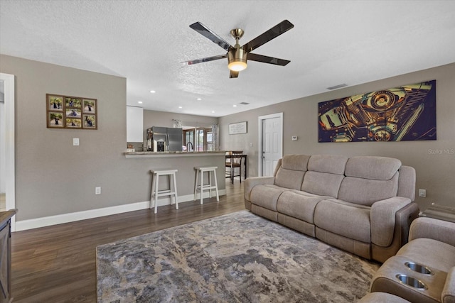 living room with ceiling fan, dark hardwood / wood-style flooring, and a textured ceiling