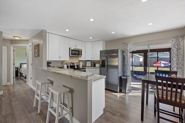 kitchen featuring kitchen peninsula, appliances with stainless steel finishes, a textured ceiling, light hardwood / wood-style flooring, and white cabinets