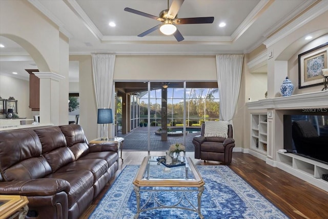 living room with a tray ceiling, ceiling fan, dark hardwood / wood-style flooring, and ornamental molding