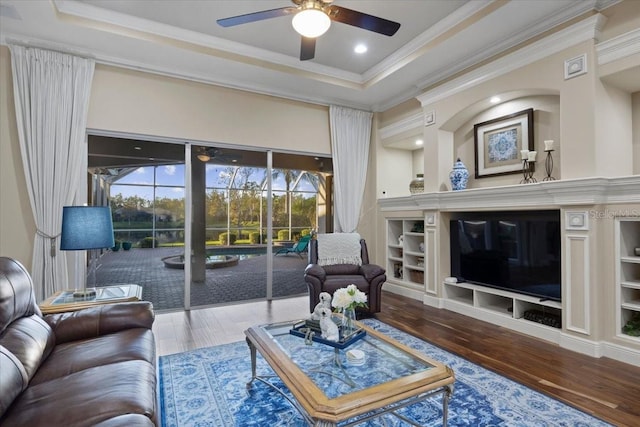 living room with ceiling fan, a raised ceiling, wood-type flooring, and ornamental molding