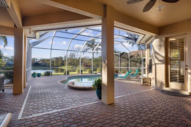 view of patio with a water view, glass enclosure, and ceiling fan