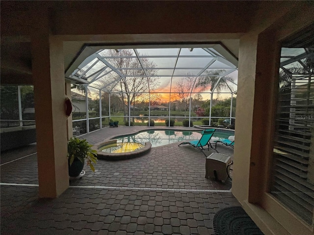 patio terrace at dusk featuring a pool with hot tub and a lanai