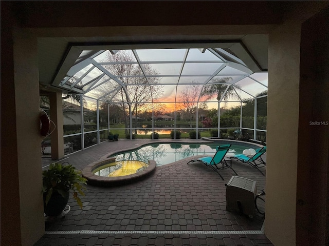 patio terrace at dusk featuring a swimming pool with hot tub and a lanai