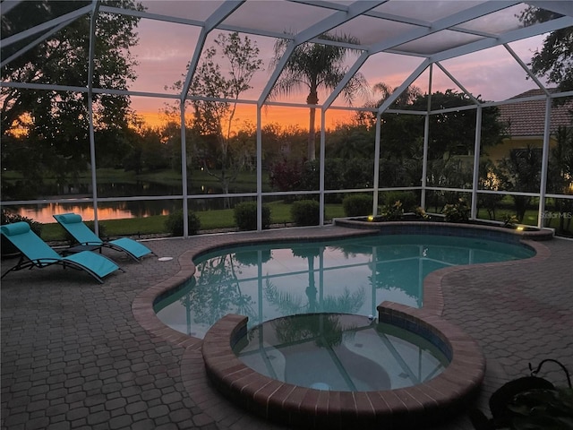 pool at dusk with an in ground hot tub, a water view, a lanai, and a patio area