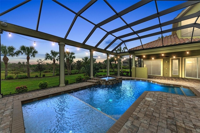 pool at dusk with an in ground hot tub, a patio area, a lanai, and a lawn