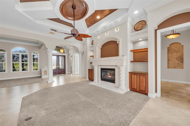 unfurnished living room featuring ceiling fan, ornamental molding, a premium fireplace, ornate columns, and light tile patterned flooring