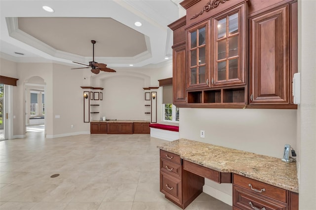 kitchen with ceiling fan, a raised ceiling, built in desk, and crown molding