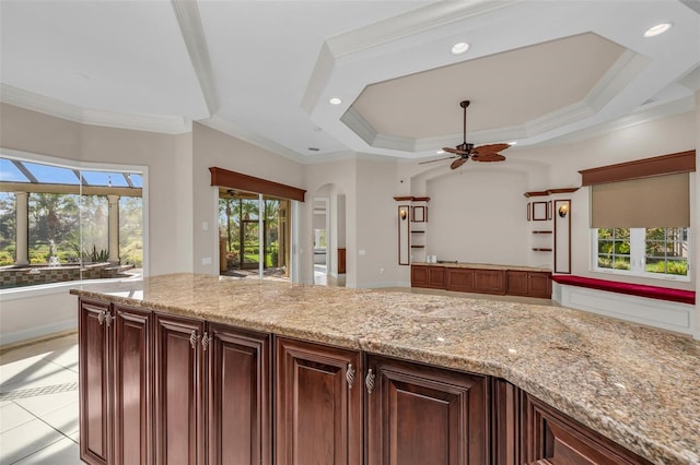 kitchen featuring ceiling fan, a raised ceiling, ornamental molding, and light stone counters