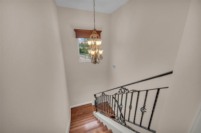 staircase with hardwood / wood-style floors and a chandelier