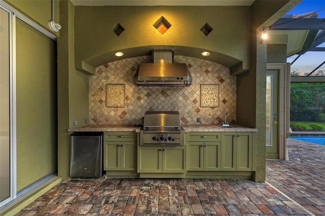 bar featuring tile counters, fridge, wall chimney range hood, and green cabinets