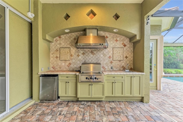 kitchen featuring fridge, wall chimney exhaust hood, tile countertops, and backsplash