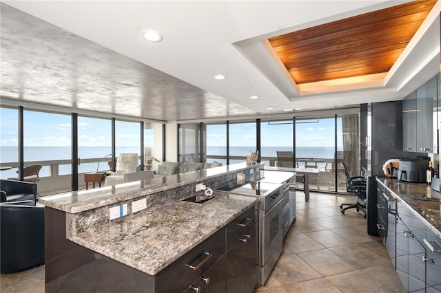 kitchen featuring dark stone counters, a large island, a raised ceiling, a water view, and electric stove