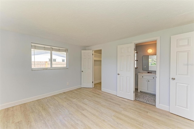 unfurnished bedroom with a textured ceiling, a spacious closet, connected bathroom, light hardwood / wood-style floors, and a closet