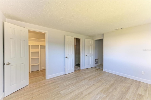 unfurnished bedroom featuring a textured ceiling, light hardwood / wood-style flooring, a spacious closet, and a closet