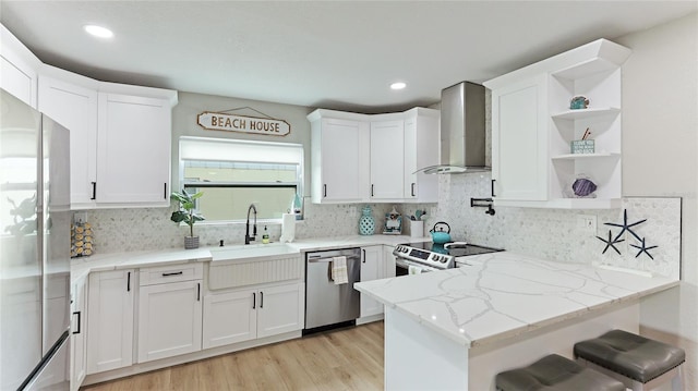 kitchen with light stone countertops, wall chimney exhaust hood, stainless steel appliances, sink, and white cabinetry