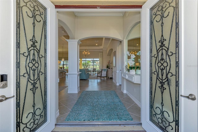 foyer entrance with tile patterned flooring, a chandelier, crown molding, and decorative columns