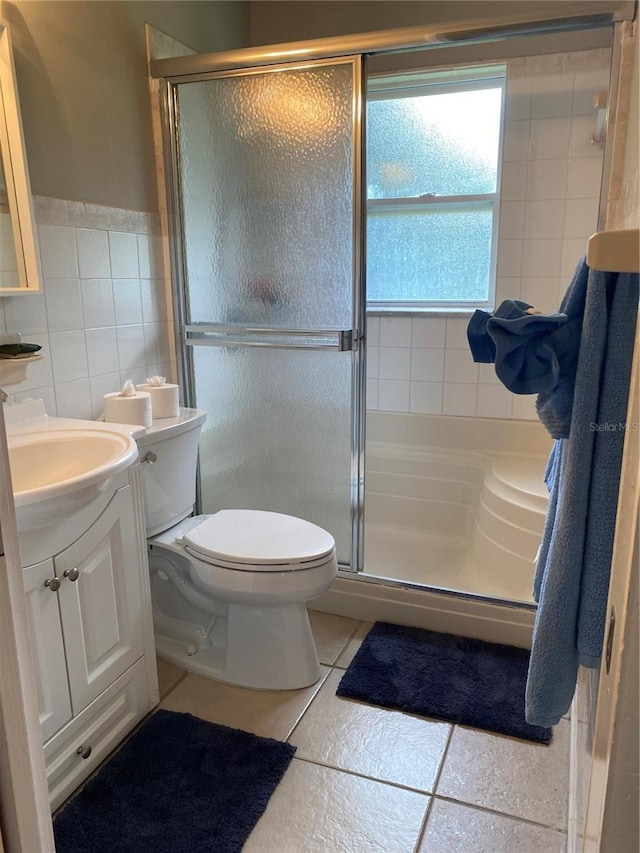 bathroom featuring tile patterned floors, toilet, vanity, a shower with shower door, and tile walls