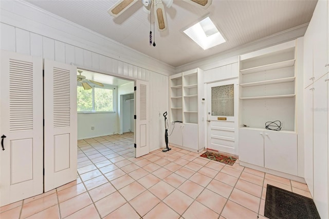 kitchen with a skylight, ceiling fan, wooden walls, light tile patterned floors, and ornamental molding