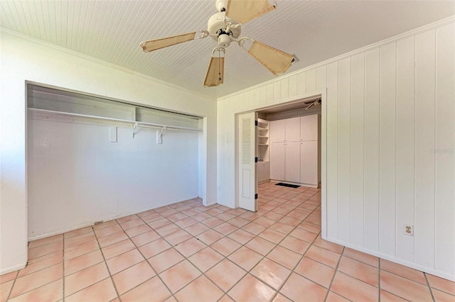 unfurnished bedroom with crown molding, wooden walls, ceiling fan, light tile patterned floors, and a closet