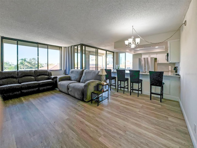 living room featuring a chandelier, light hardwood / wood-style floors, a textured ceiling, and a wall of windows