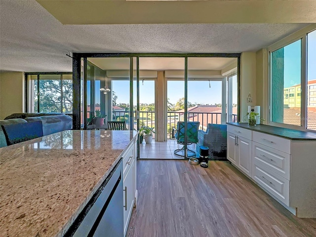 kitchen featuring light stone counters, white cabinets, a textured ceiling, and light wood-type flooring