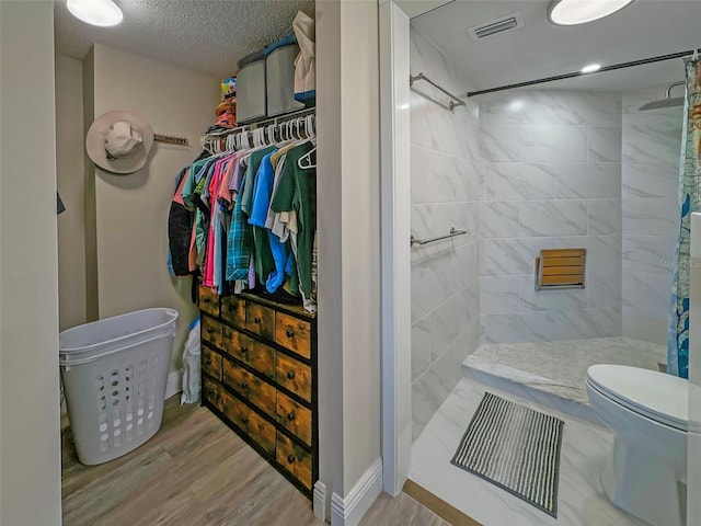 bathroom featuring hardwood / wood-style flooring, toilet, tiled shower, and a textured ceiling