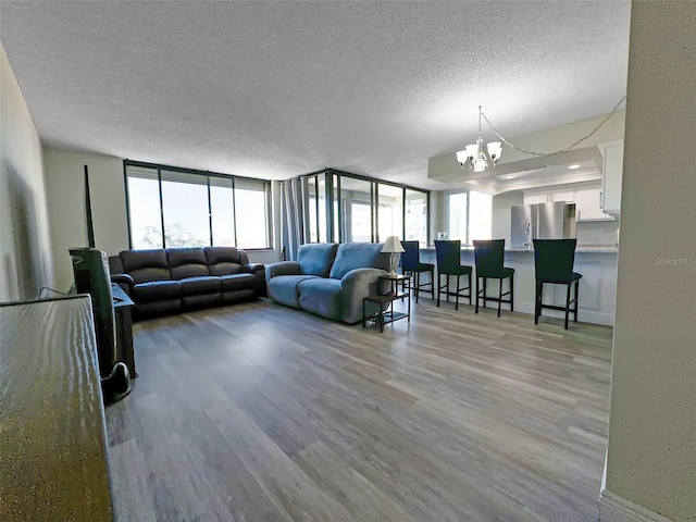 living room featuring light wood-style floors, floor to ceiling windows, a textured ceiling, and an inviting chandelier