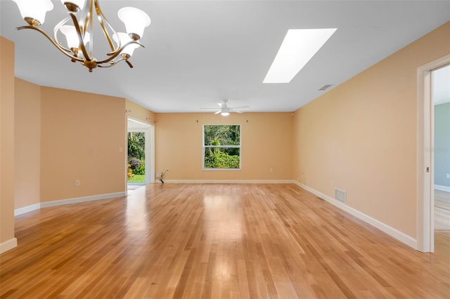 empty room featuring a skylight, light hardwood / wood-style floors, and ceiling fan with notable chandelier