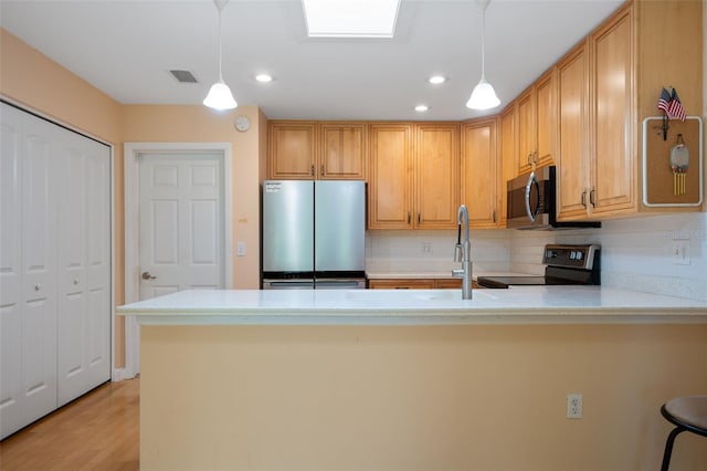 kitchen featuring decorative backsplash, stainless steel appliances, hanging light fixtures, and light hardwood / wood-style flooring