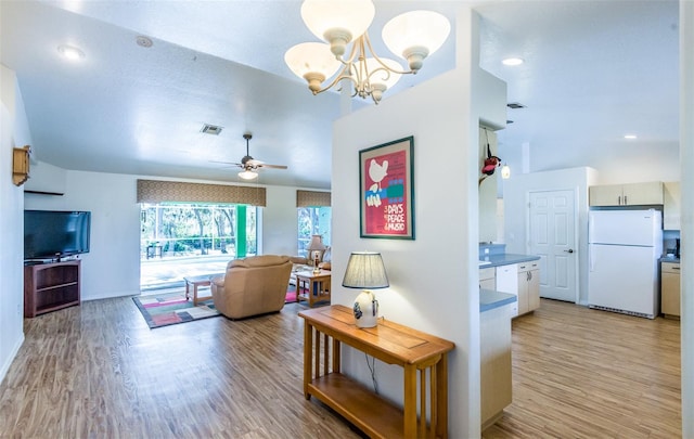 living room with ceiling fan with notable chandelier, light wood-style flooring, and visible vents