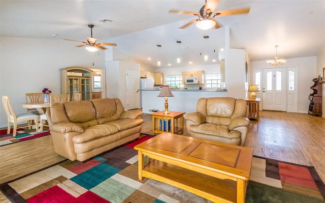 living area featuring vaulted ceiling, ceiling fan with notable chandelier, wood finished floors, and visible vents