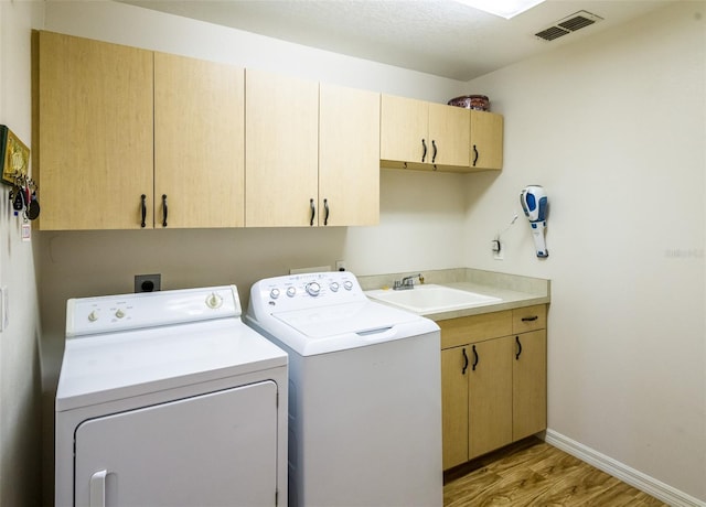 washroom with cabinet space, visible vents, light wood-style flooring, a sink, and washer and dryer