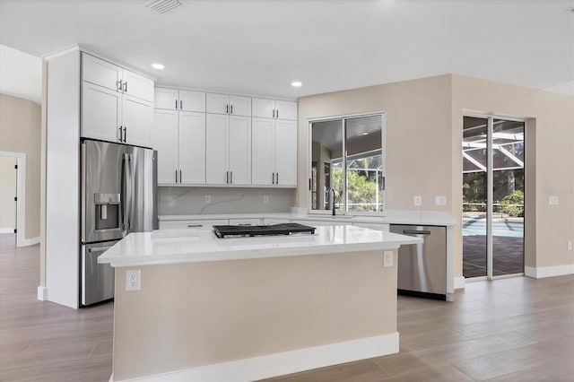 kitchen with white cabinets, a center island, stainless steel appliances, and light hardwood / wood-style flooring