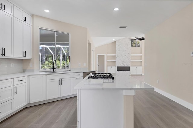 kitchen with ceiling fan, sink, white cabinets, a kitchen island, and stainless steel gas stovetop