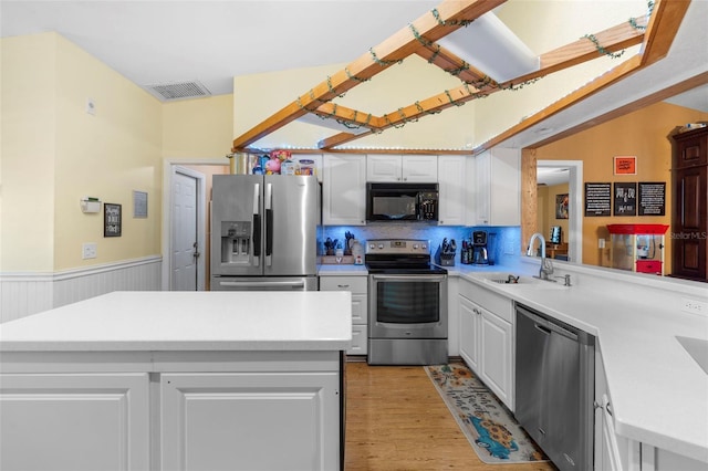 kitchen with kitchen peninsula, appliances with stainless steel finishes, sink, white cabinets, and light hardwood / wood-style floors