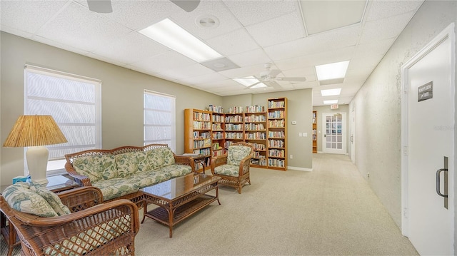 living area with a drop ceiling, ceiling fan, and light carpet