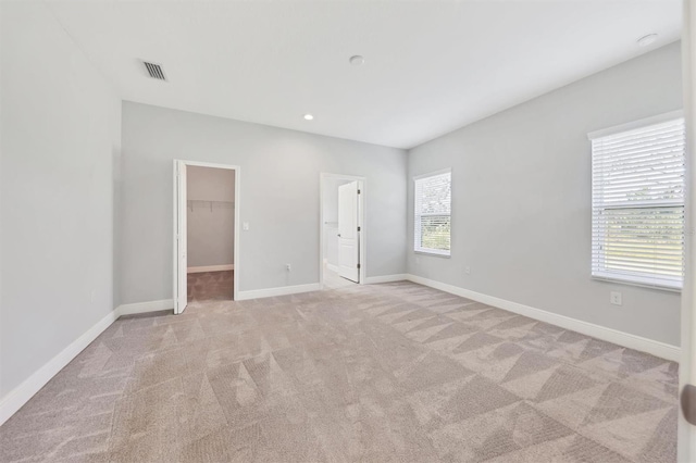 unfurnished bedroom with a walk in closet, a closet, light colored carpet, and multiple windows